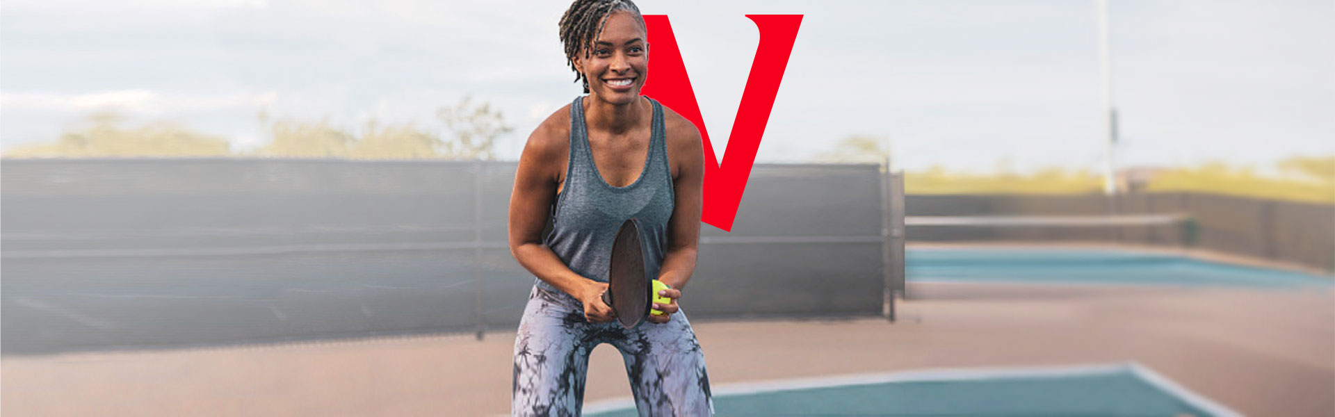 Person smiling while standing on a court, playing pickle ball. 