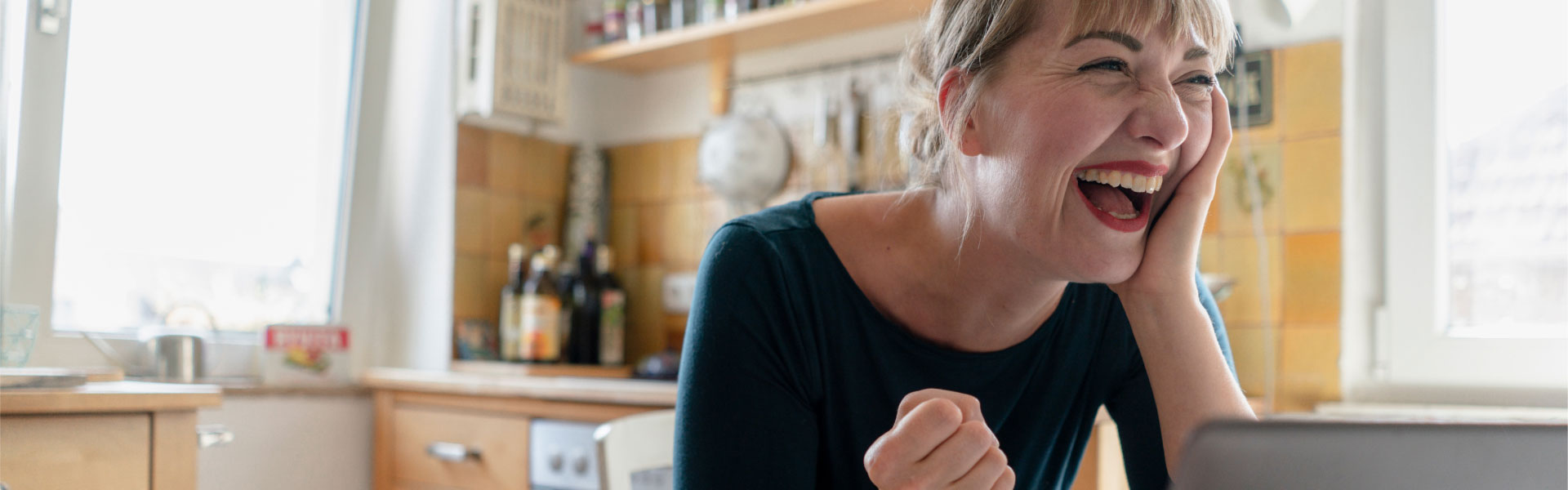 Laughing blonde woman seated at kitchen table.