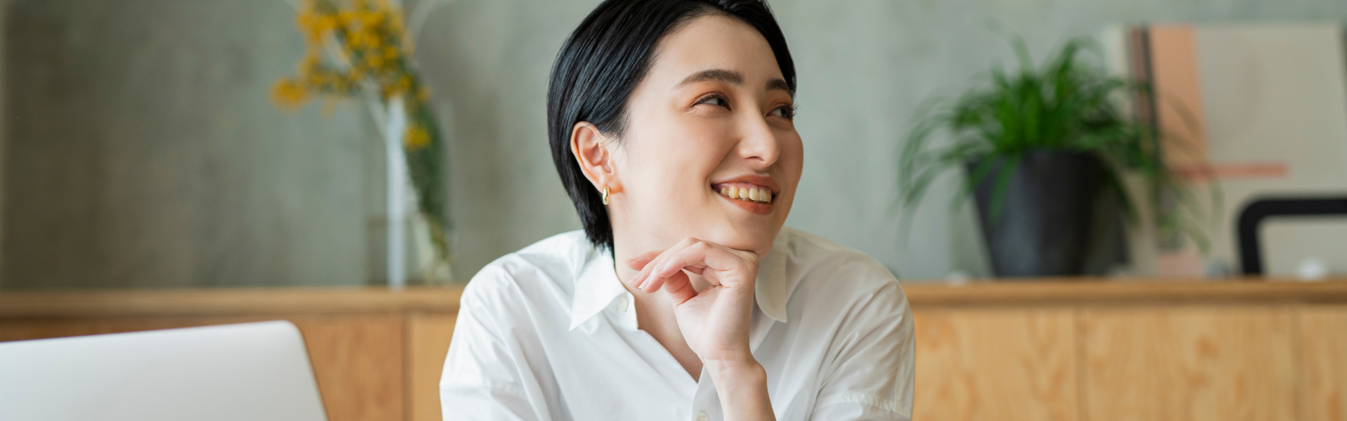 A young woman is resting her chin on her hand while smiling at someone out of the frame.
