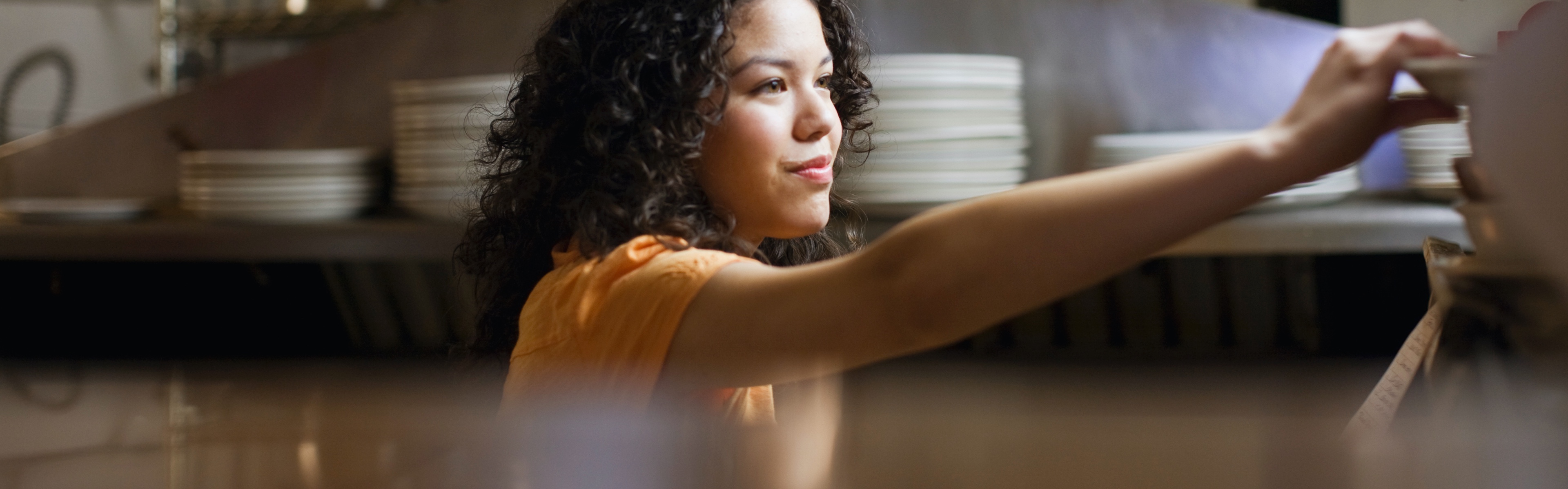 A young waitress is grabbing a plate in a restaurant’s kitchen.