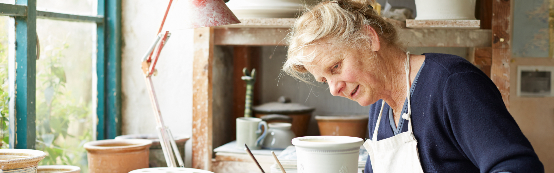 An older woman is looking at pottery work in front of her.