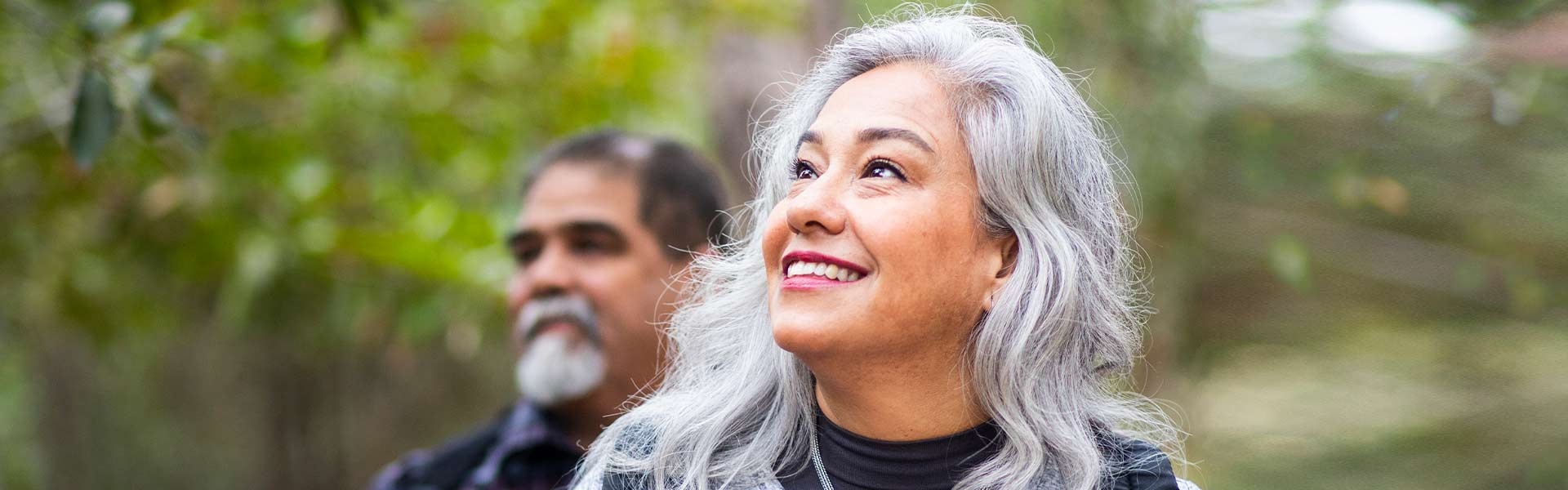 An older man and woman are smiling while hiking in the woods.