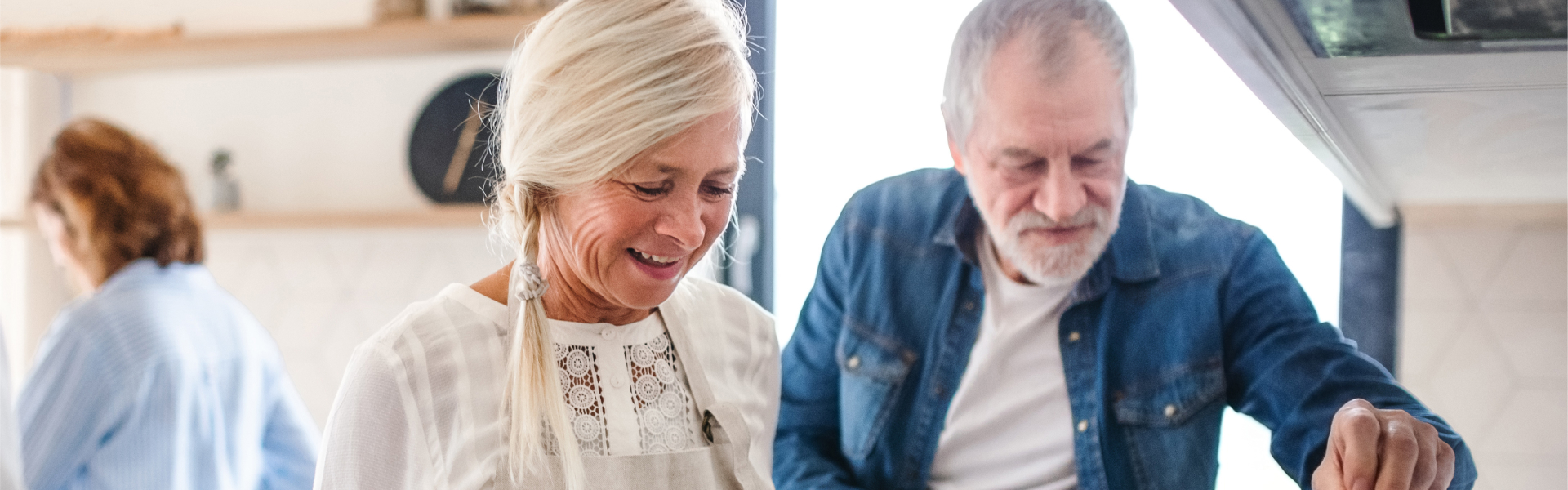 Retired couple cooking together in kitchen, under oven hood.