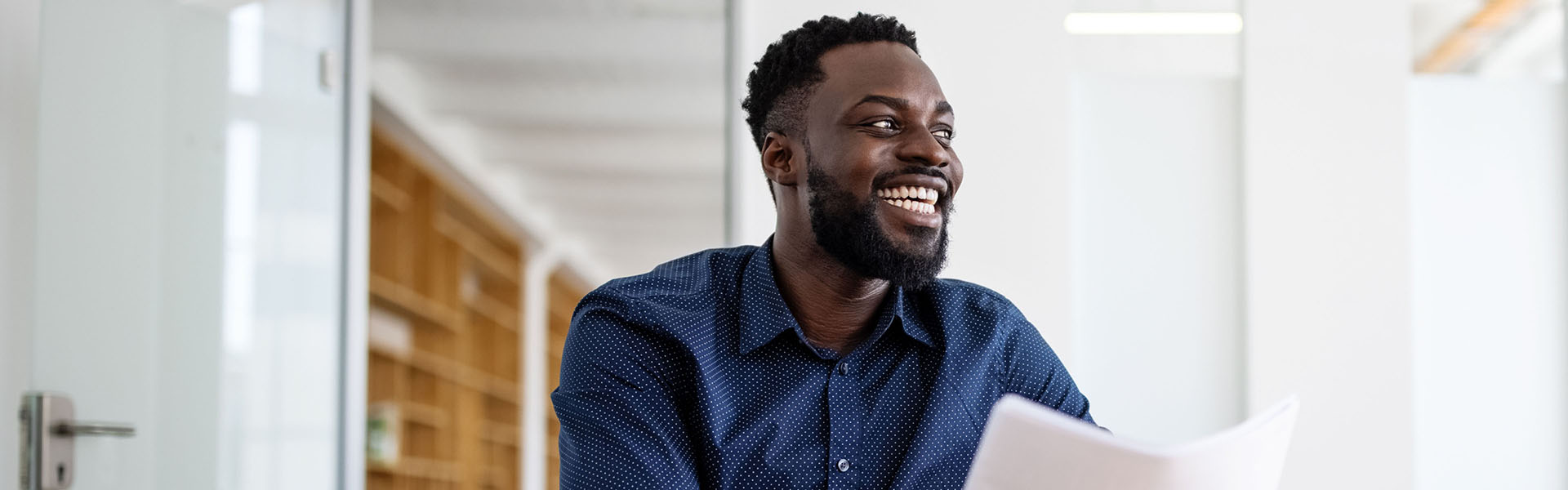 Smiling man seated at conference table with papers in his hands.